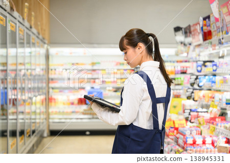 A female store clerk at the supermarket holding a tablet 138945331