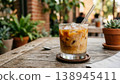 An iced latte sits on a wooden table at a terrace cafe, its milk creating a beautiful marbled pattern. 138945411