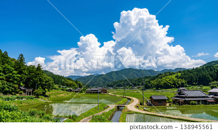 A quintessential Japanese landscape of summer, with towering cumulonimbus clouds and rice paddies, and a mountain village dotted with torii gates and old farmhouses. 138945561