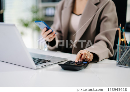 Women counting coins on calculator taking from the piggy bank. hand holding pen working on calculator to calculate on desk about cost Women counting coins on calculator taking from the piggy bank. hand holding pen working on calculator to calculate on desk about cost 138945618
