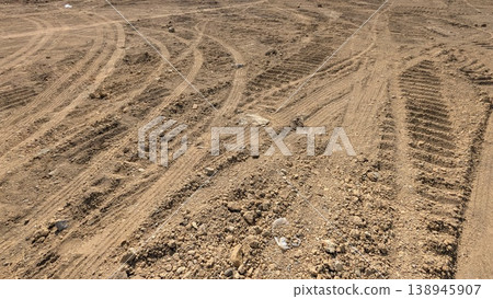 Tire tracks mark dry, sandy soil. Parallel grooves create a rhythmic pattern across parched ground. High angle view highlights industrial or agricultural movement on rough, dusty terrain. Tire tracks mark dry, sandy soil. Parallel grooves create a rhythmic pattern across parched ground. High angle view highlights industrial or agricultural movement on rough, dusty terrain. 138945907