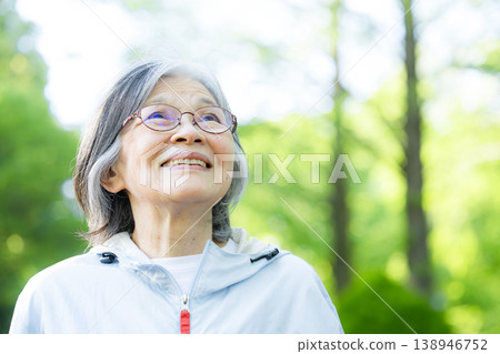 A smiling, active senior woman exercising in a park surrounded by fresh greenery; walking and running are popular sports for maintaining health. A smiling, active senior woman exercising in a park surrounded by fresh greenery; walking and running are popular sports for maintaining health. 138946752