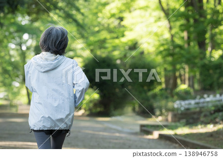 A smiling, active senior woman exercising in a park surrounded by fresh greenery; walking as a sport to maintain health (face not shown) A smiling, active senior woman exercising in a park surrounded by fresh greenery; walking as a sport to maintain health (face not shown) 138946758