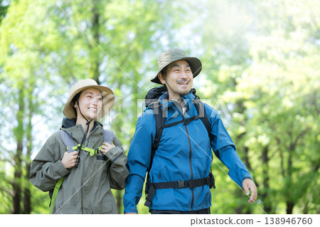 A close-up of a smiling couple walking through a lush spring forest, an image of outdoor activities such as hiking and trekking. A close-up of a smiling couple walking through a lush spring forest, an image of outdoor activities such as hiking and trekking. 138946760