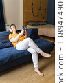 Woman wearing headphones sitting on a blue sofa, enjoying music, surfing the internet and using a smartphone in her cozy living room 138947490