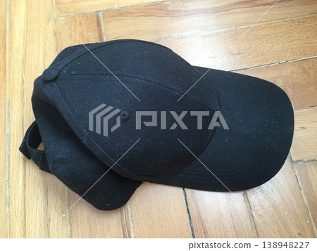 Black baseball cap resting on a wooden floor in a quiet room during the afternoon 138948227