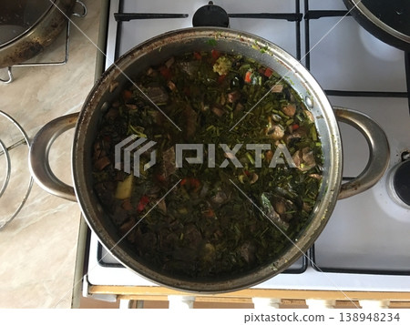 Cooking a traditional dish in a pot on a stove with fresh ingredients in a kitchen setting during the day Cooking a traditional dish in a pot on a stove with fresh ingredients in a kitchen setting during the day 138948234