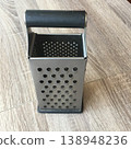 Kitchen tool used for grating cheese placed on wooden table in bright light during day 138948236