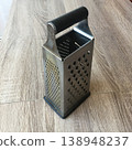 Kitchen grater placed on wooden table near food preparation area during daylight hours 138948237