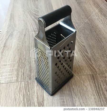 Kitchen grater placed on wooden table near food preparation area during daylight hours 138948237