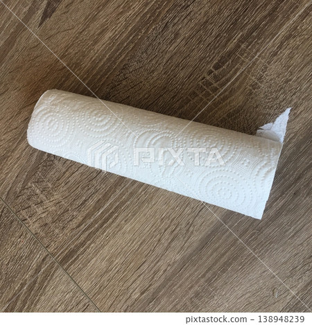 Roll of paper towels placed on wooden floor in kitchen used for cleaning spills and messes during daily chores or cooking tasks Roll of paper towels placed on wooden floor in kitchen used for cleaning spills and messes during daily chores or cooking tasks 138948239