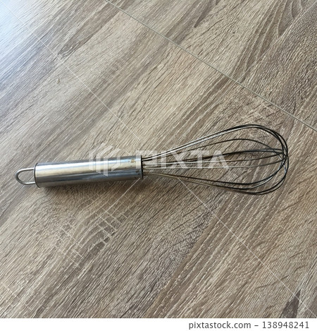 Metal whisk on a wooden surface in a kitchen setting during daylight 138948241
