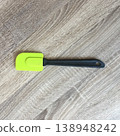 Bright silicone spatula rests on wooden kitchen surface near cooking area while preparing food during daytime in a home setting 138948242