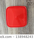 Red plastic container lid placed on a wooden surface in a bright kitchen setting during daytime 138948243
