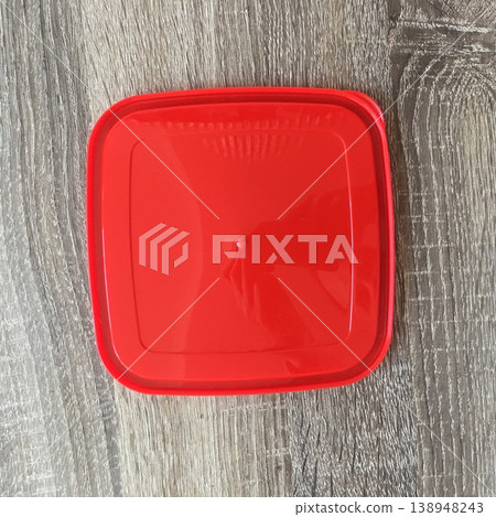 Red plastic container lid placed on a wooden surface in a bright kitchen setting during daytime Red plastic container lid placed on a wooden surface in a bright kitchen setting during daytime 138948243