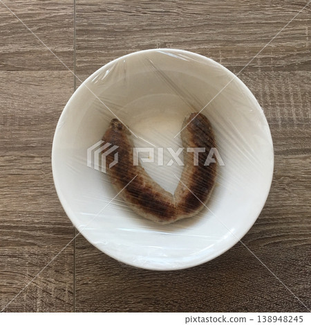 Sausages wrapped in plastic inside a white bowl on a wooden table surface 138948245