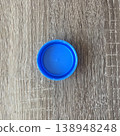Small blue lid placed on a wooden surface in a well-lit room during daytime showing minimal shadows 138948248