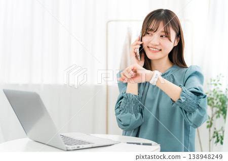 一位時尚的年輕亞洲女性一邊使用電腦，一邊用智慧型手機通話 138948249
