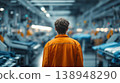 Worker in orange standing in a factory among machines during daytime 138948290