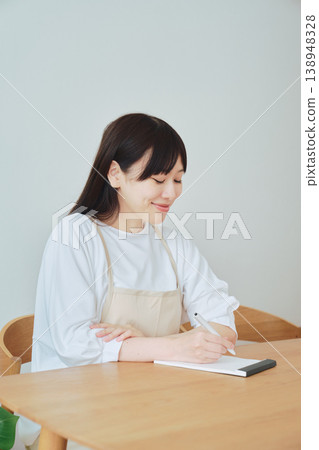 A woman is taking notes on the menu; a scene depicting meal preparation and daily planning. A woman is taking notes on the menu; a scene depicting meal preparation and daily planning. 138948328