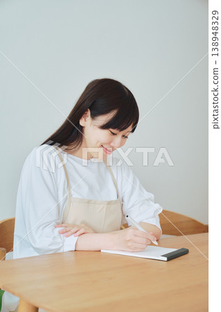 A woman is taking notes on the menu; a scene depicting meal preparation and daily planning. A woman is taking notes on the menu; a scene depicting meal preparation and daily planning. 138948329