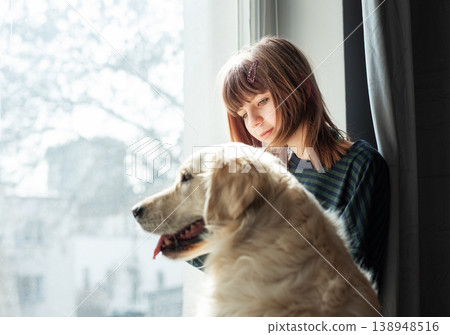 Girl and golden retriever dog looking out window 138948516