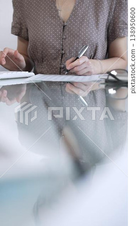 Businesswoman accountant, wearing brawn dotted blouse, is using a calculator at sleek glass desk in a contemporary office, vertical view. Taxes, audit in business Businesswoman accountant, wearing brawn dotted blouse, is using a calculator at sleek glass desk in a contemporary office, vertical view. Taxes, audit in business 138950600
