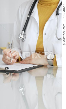 Female physician or medic completing paperwork, preparing a diagnosis, or providing healthcare service in a clean modern office. Medicine, healthcare and science concept 138950643