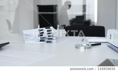 Office desk with stack of paper and magnifying glass, symbolizing heavy bureaucracy and business workload. Audit and taxes in business 138950650
