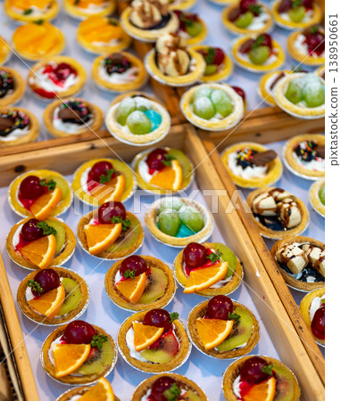 Assorted dessert cups with fruit and chocolate displayed in market stall, colorful sweet selection with orange kiwi grapes and mango, ready for sale in street food setting Assorted dessert cups with fruit and chocolate displayed in market stall, colorful sweet selection with orange kiwi grapes and mango, ready for sale in street food setting 138950661
