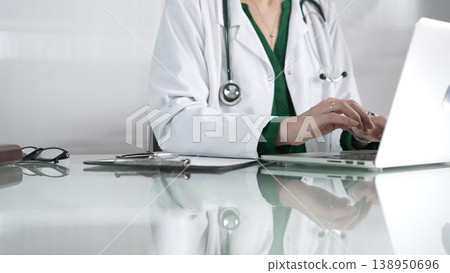 Doctor woman using technology in healthcare, close up of hands typing on laptop with stethoscope, glasses, and clipboard on glass desk. Medicine concept Doctor woman using technology in healthcare, close up of hands typing on laptop with stethoscope, glasses, and clipboard on glass desk. Medicine concept 138950696