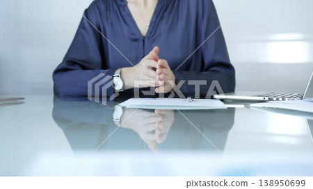 Businesswoman, wearing blue blouse, is signing a contract on glass desk with laptop and documents in office background. Business people concept 138950699