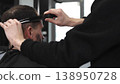 Skilled barber trimming client's hair using professional scissors, creating precise hairstyle in contemporary salon with modern interior and relaxed atmosphere 138950728