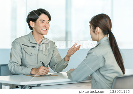 Male and female manufacturing and factory workers in work clothes holding a meeting/discussion in a conference room. Male and female manufacturing and factory workers in work clothes holding a meeting/discussion in a conference room. 138951155