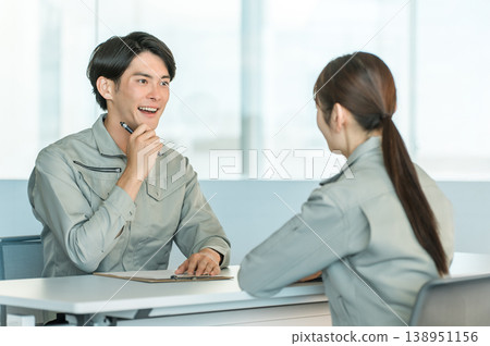 Male and female manufacturing and factory workers in work clothes holding a meeting/discussion in a conference room. Male and female manufacturing and factory workers in work clothes holding a meeting/discussion in a conference room. 138951156