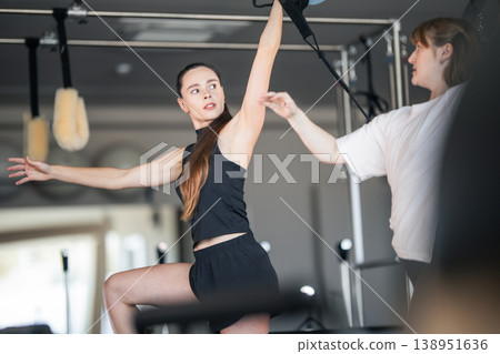 Woman practicing pilates exercise receiving personal instructor guidance 138951636