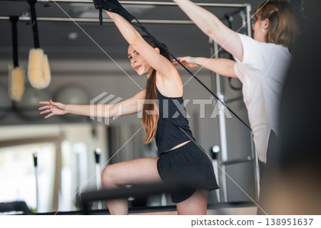 Woman training on pilates reformer with instructor assistance Woman training on pilates reformer with instructor assistance 138951637