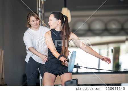 Woman exercising on pilates reformer with trainer guidance 138951640