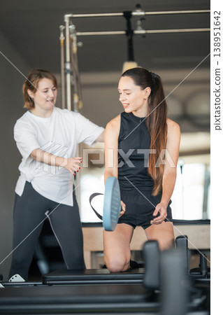Woman exercising on pilates reformer receiving instruction Woman exercising on pilates reformer receiving instruction 138951642