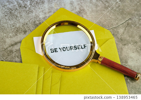 Magnifying glass on a yellow envelope reveals BE YOURSELF on white paper, placed on a gray concrete surface indoors during the day Magnifying glass on a yellow envelope reveals BE YOURSELF on white paper, placed on a gray concrete surface indoors during the day 138953465