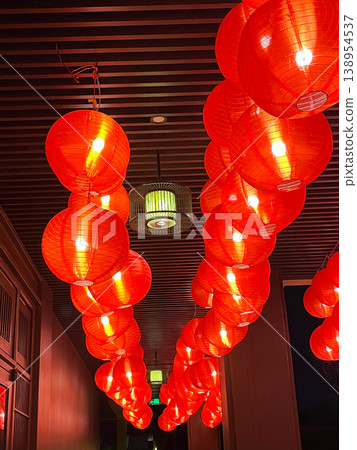 Glowing round red paper lanterns hanging in rows from a dark slatted wooden ceiling for Asian cultural events and interior design decoration themes 138954537