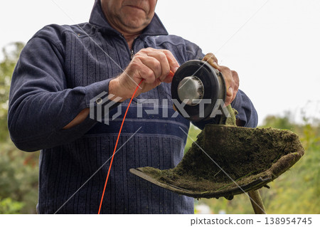 Man changing trimmer line on string trimmer head. Gardener maintenance of garden lawn mower tool. Handyman perform repair of power equipment. Landscaping work and summer gardening chore. 138954745