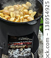 Cooking potatoes in a cast iron pot over an open flame in a backyard setting near green grass 138954925