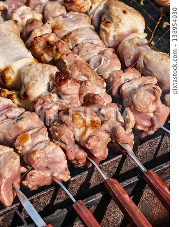 Grilling meat on skewers in an outdoor setting during a sunny day in a backyard barbecue Grilling meat on skewers in an outdoor setting during a sunny day in a backyard barbecue 138954930