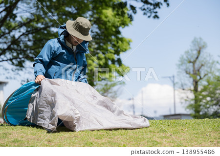 A scene of a man setting up a tent while camping, preparing for the outdoors. 138955486
