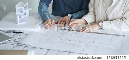 Architects working together, developing a building design by assembling a scale model and reviewing detailed blueprints, symbolizing teamwork, planning, and architectural creation Architects working together, developing a building design by assembling a scale model and reviewing detailed blueprints, symbolizing teamwork, planning, and architectural creation 138955625