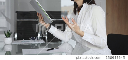 Businesswoman in a white shirt and headset leading a video call from a modern office, presenting with a tablet and gesturing as she discusses strategy and trains remote colleagues Businesswoman in a white shirt and headset leading a video call from a modern office, presenting with a tablet and gesturing as she discusses strategy and trains remote colleagues 138955645