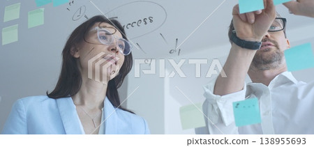 Business colleagues collaborating on an innovative project, brainstorming ideas and developing a strategic plan using sticky notes on a clear glass whiteboard 138955693