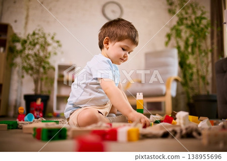 Little boy building structure with plastic blocks sitting on floor in modern living room Little boy building structure with plastic blocks sitting on floor in modern living room 138955696