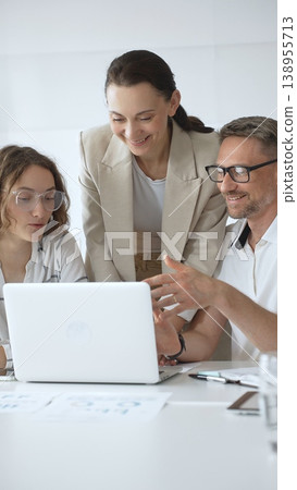 Business people working together, reviewing data on laptop screen, sharing insights during collaborative office meeting, emphasizing professional teamwork 138955713
